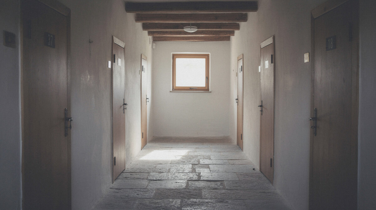 Un couloir d'hôtellerie monastique, portes de bois numérotées, une fenêtre au fond
