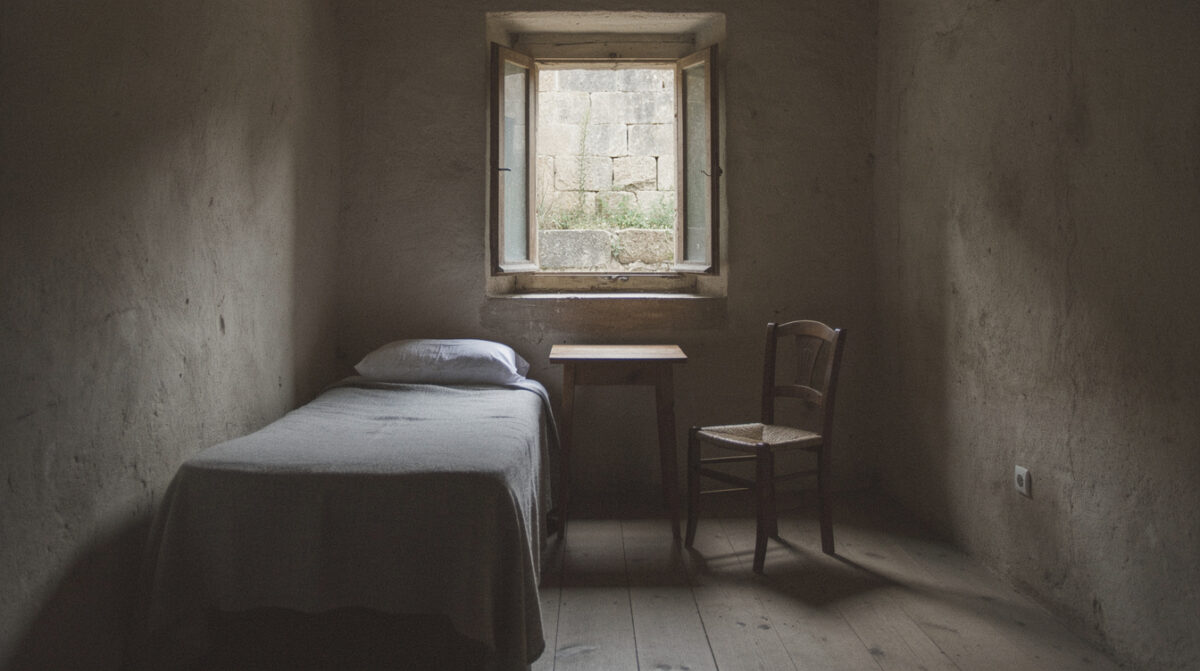 Une chambre d'hôtellerie monastique : un lit, une table, une chaise, une fenêtre sur la cour